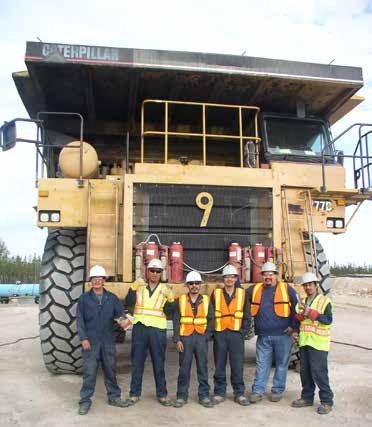 Six trainees in high-visibility clothing standing in front of the wheel of a Caterpillar 777 articulated haul truck, which is roughly twice their height.